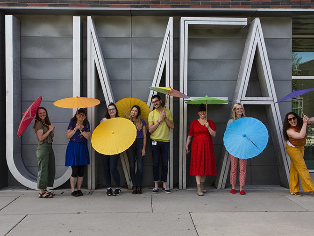Utah Museum of Fine Arts staff in front of UMFA sign holding rainbow umbrellas