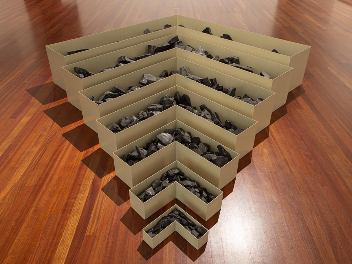 Robert Smithson, Nonsite, Site Uncertain, 1968 A set of 7 nested V-shaped cream colored metal boxes are lined up from small to large forming a tiered shaped meant to resemble a strip mine. They are filled with coal. Robert Smithson, Nonsite, Site Uncertain, 1968