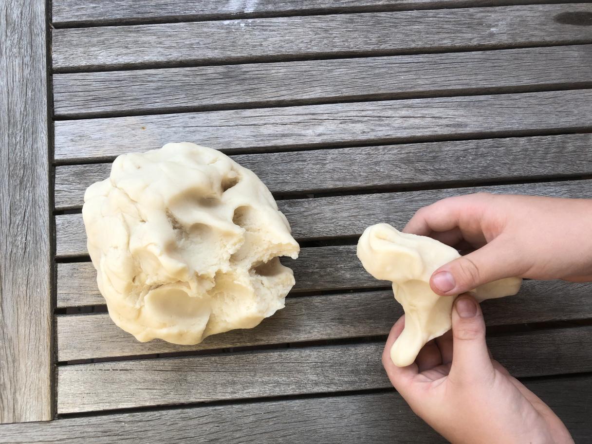 a mound fo salt dough sits next to a pair of hand that hold a piece of dough