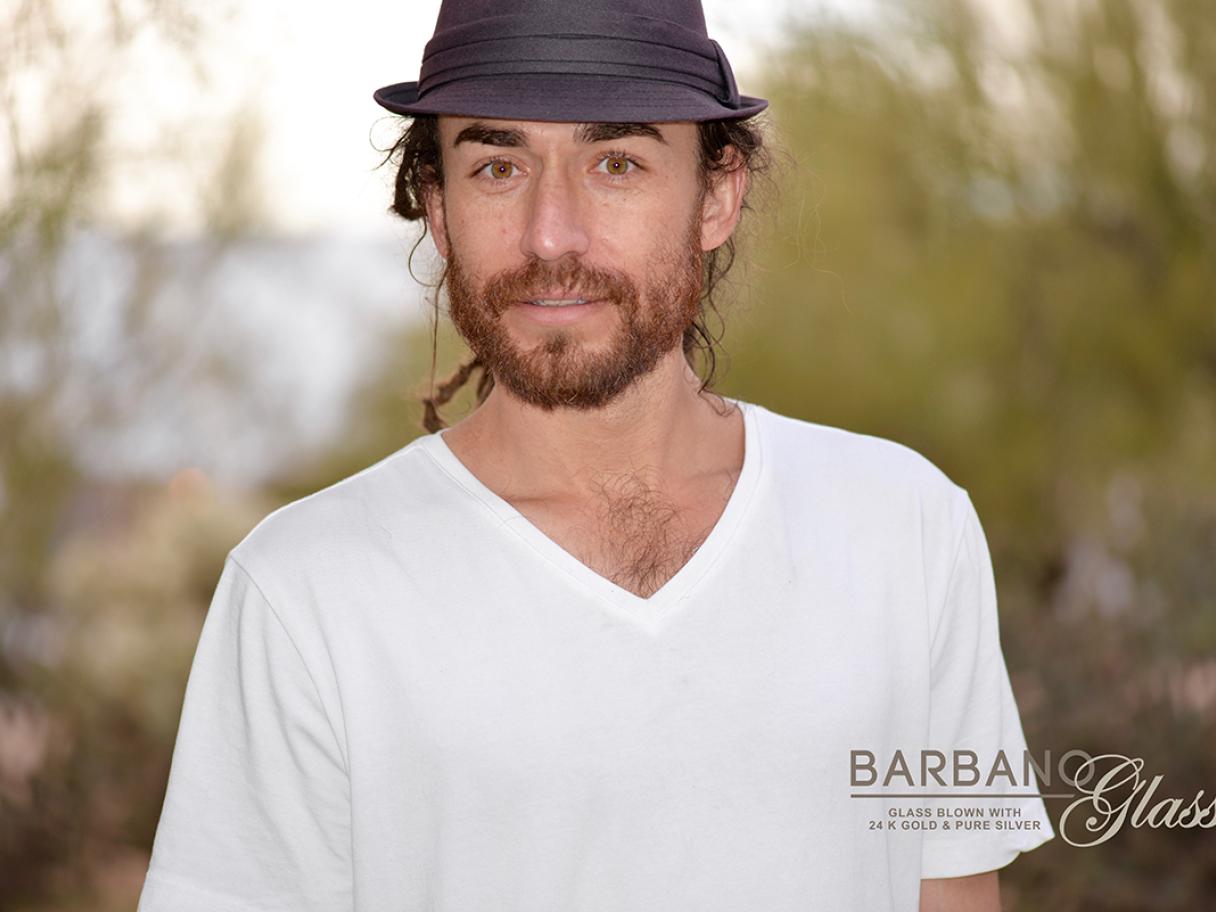 Anthony Barbano headshot white man in white v-neck tee-shirt and black fedora has has a short beard 