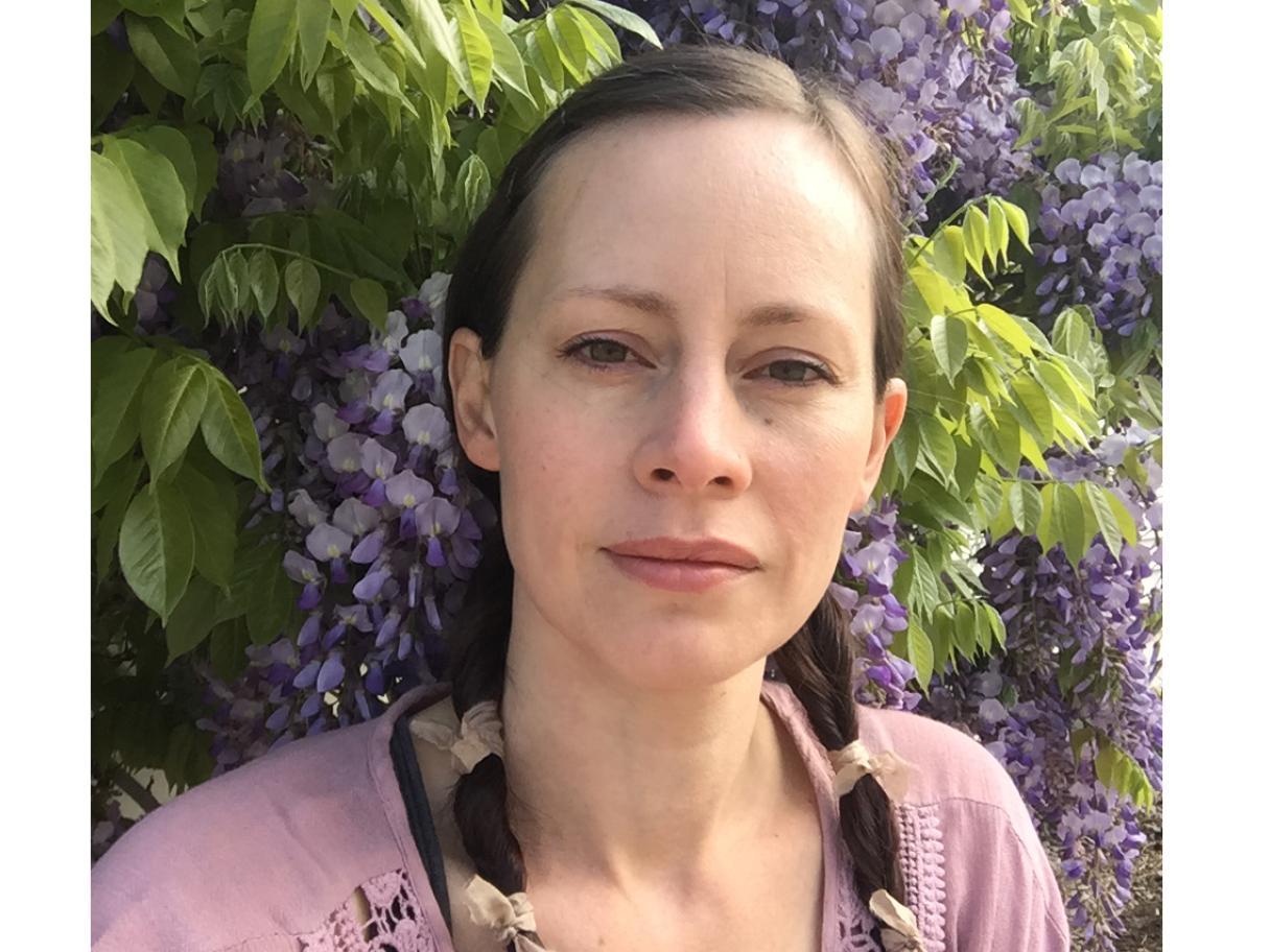 Roxanne Vigos Roxanne Vigos white woman with brown hair in two braid she stand in front of a hedge of purple flowers
