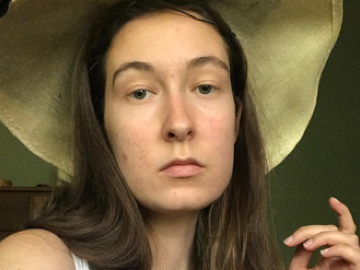 Adrienne Krueger Adrienne Krueger looks unsmiling at the camera she wears a loarge sun hat and white tank top