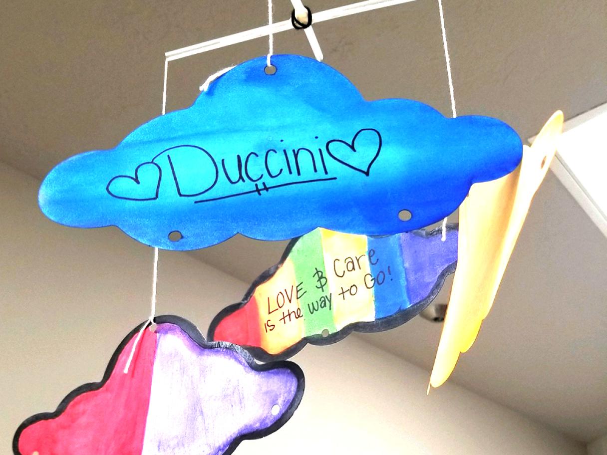 a mobile of four painted paper cut-out clouds the most prominent in front is varying shades of blue with Duccini written int he middle flaked by two hearts on with side