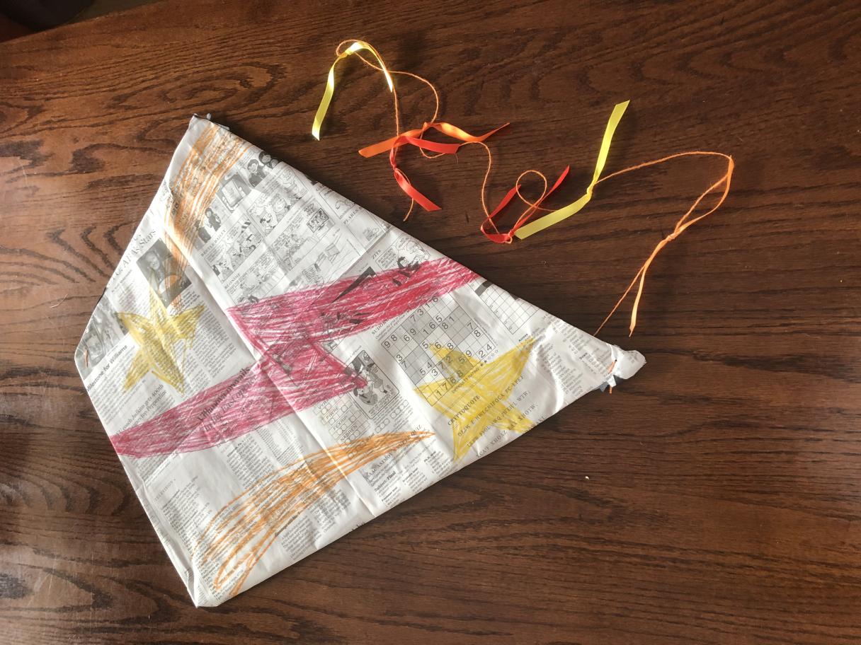 Kite made of newpaper with  a red lightning bolt draw down the middle with red, yellow and orange ribbons