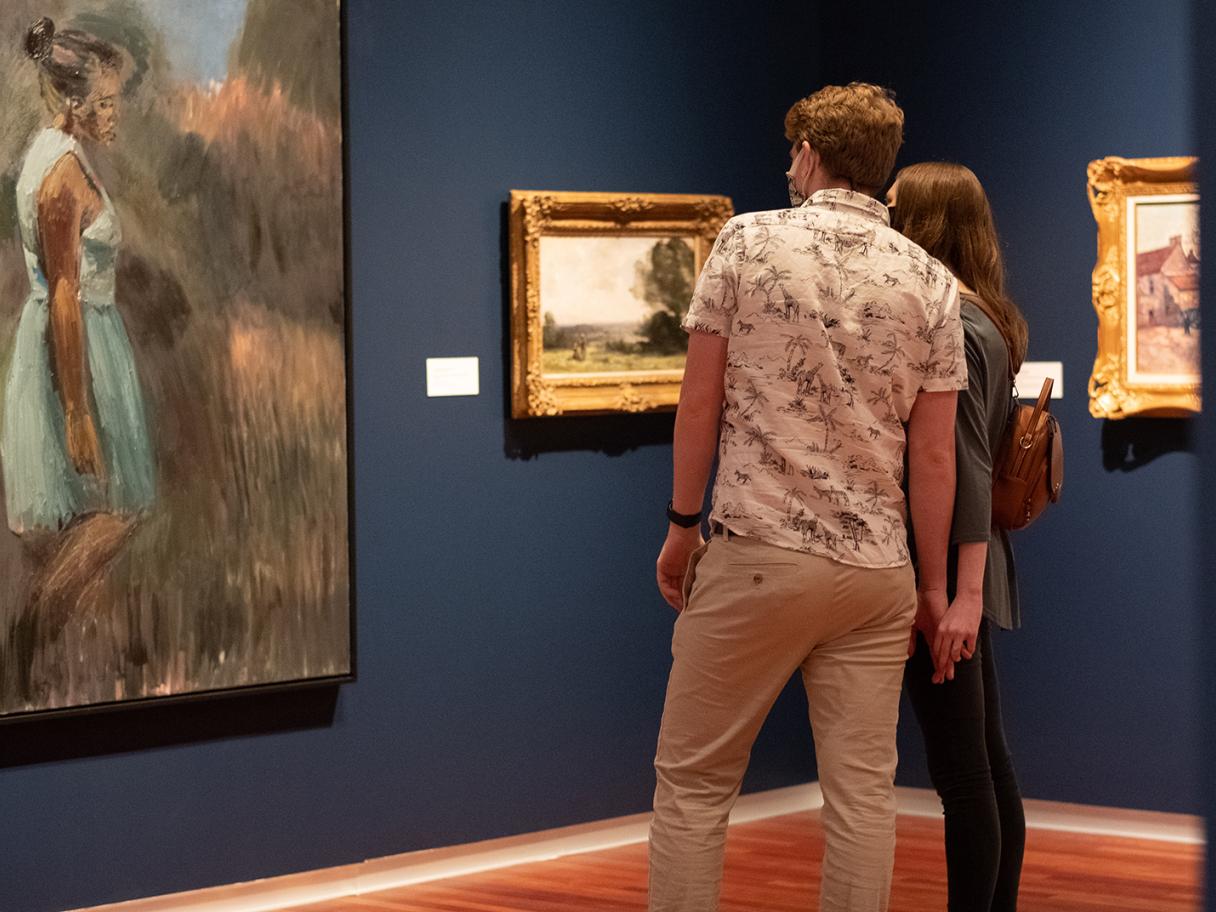 a couple with their back to the camera looks at Periphery, a painting of a woman in a filed in the UMFA European gallery