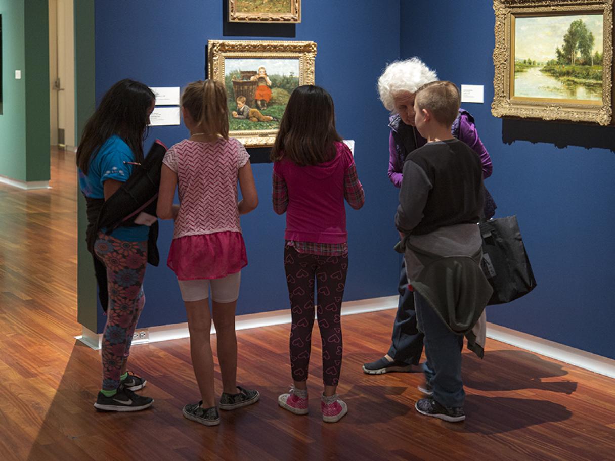four kids and a docent looking at a painting in the UMFA European gallery