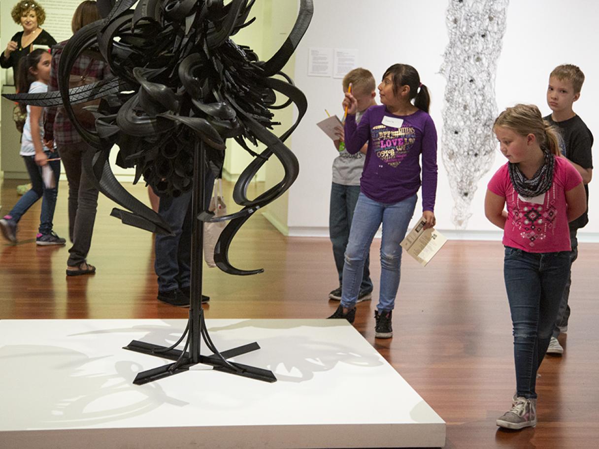 a group of five school kids look at a sculpture made of cut up as twisted tires