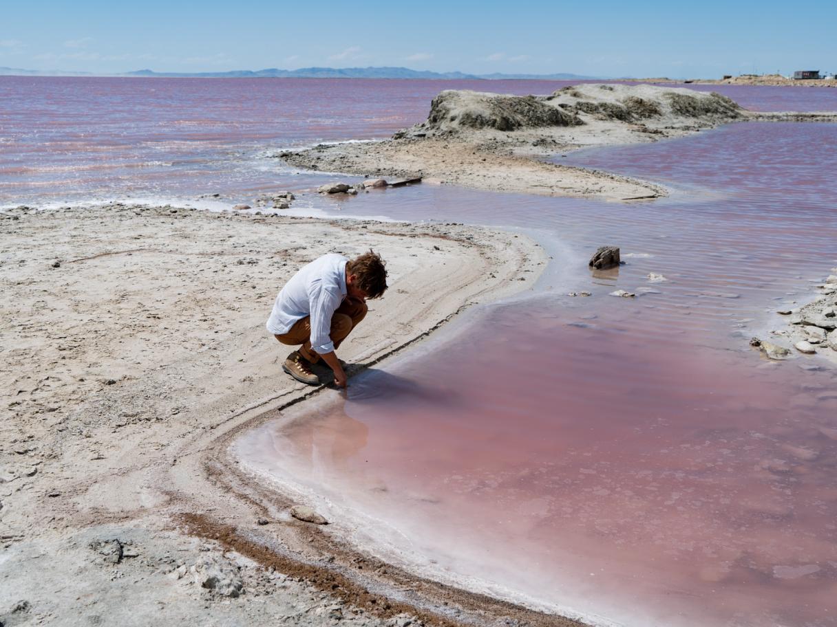 a person kneeling down to look into the pick waters of Great Salt Lake 