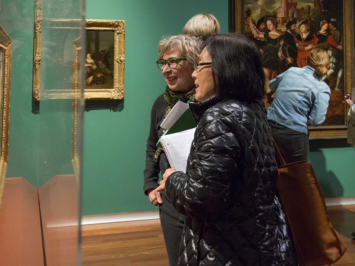 Two older women look at and discuss a work of at the UMFA