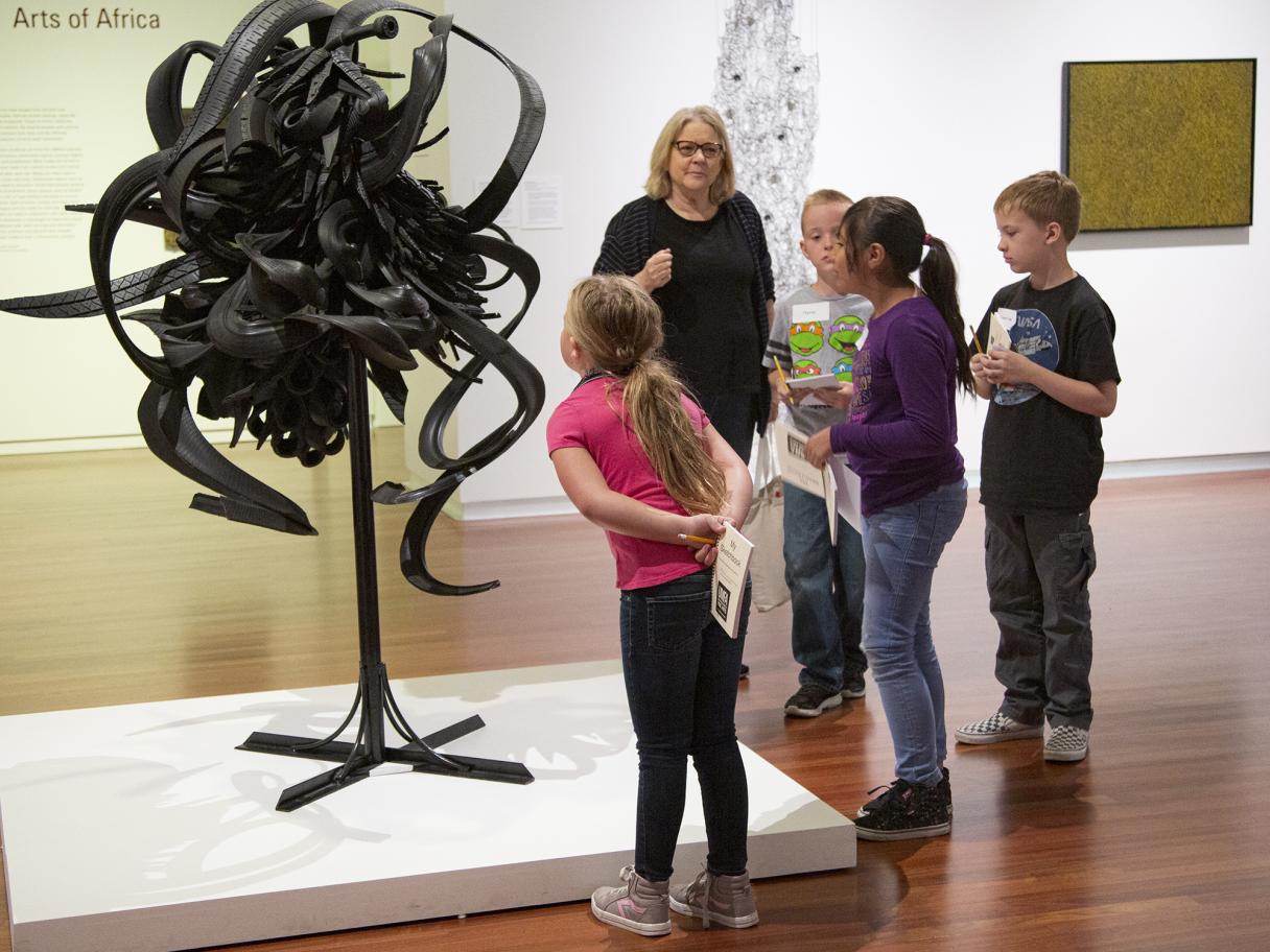 a group of children look at a sculpture made of cut up tires forming a swirling cluster shape