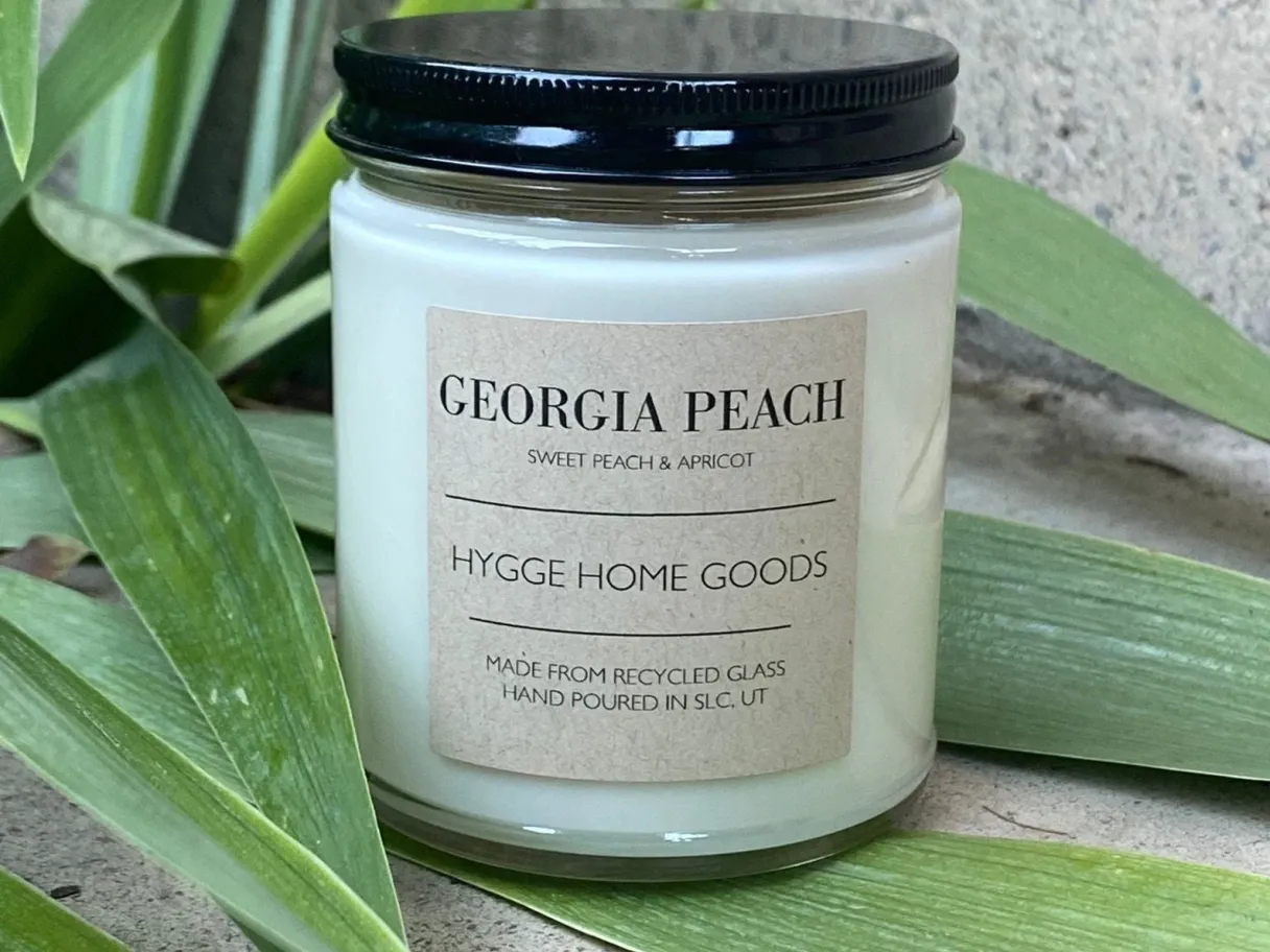 a candle in a jar, the label says Georgia Peach the jar is sitting on a large green leaf