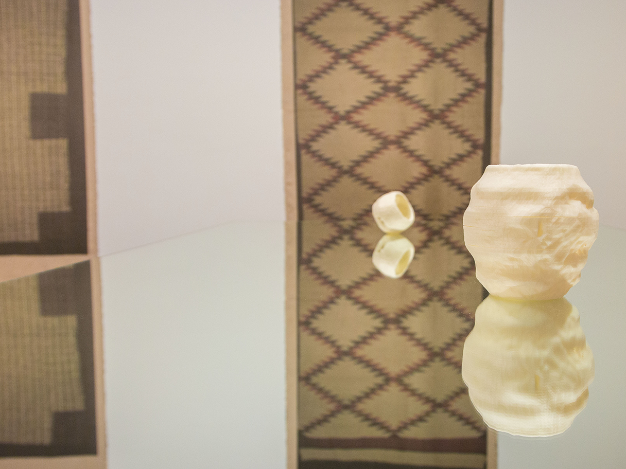 White sculptures sitting on top of a mirror and reflecting back. Brown rugs on the white walls