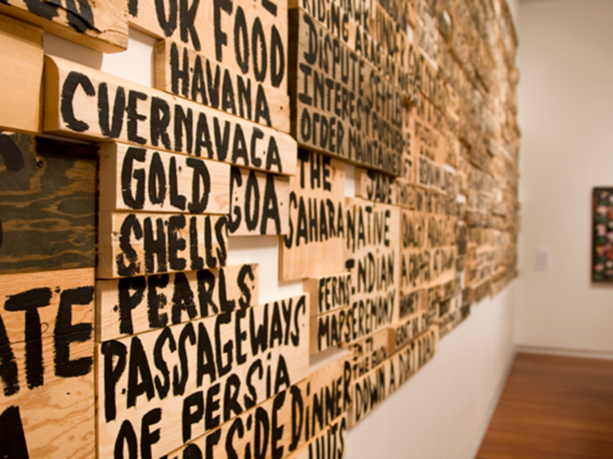 Random words written in English in thick, dark letters on light pieces of wood fixed to a white wall.