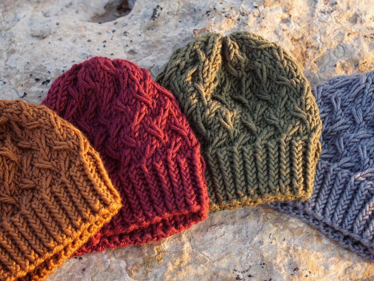 Orange, red, green and grey knitted hats lying flat on a beige, textured background
