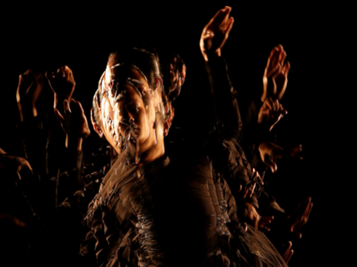 A blurred photo of a person dancing with their hands in the air with a low light source in a dark room