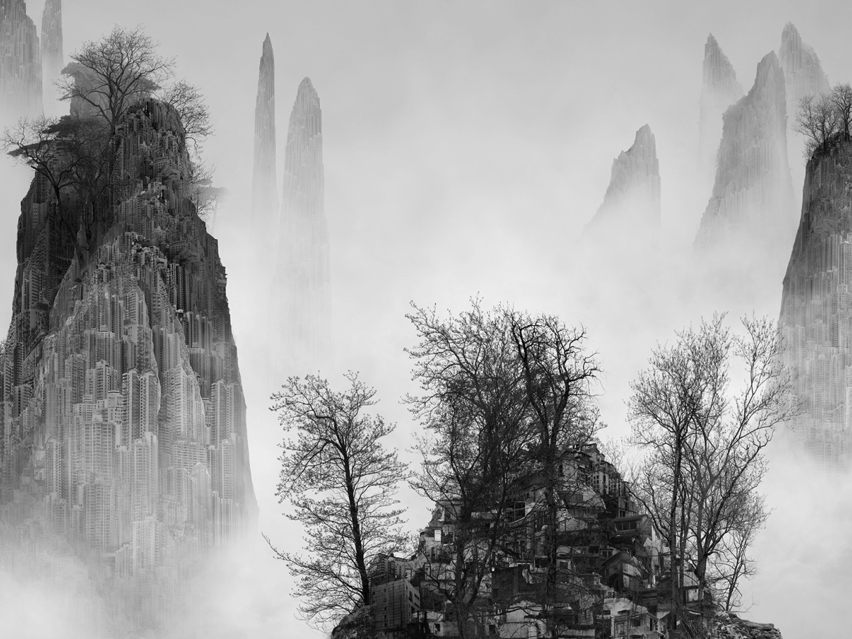 Black and white photo of tall, fog-covered hills with villages and trees
