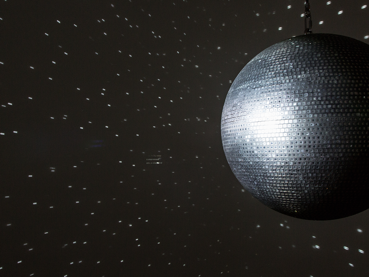 A large silver disco ball reflecting small dots of light in a dark room on dark colored walls