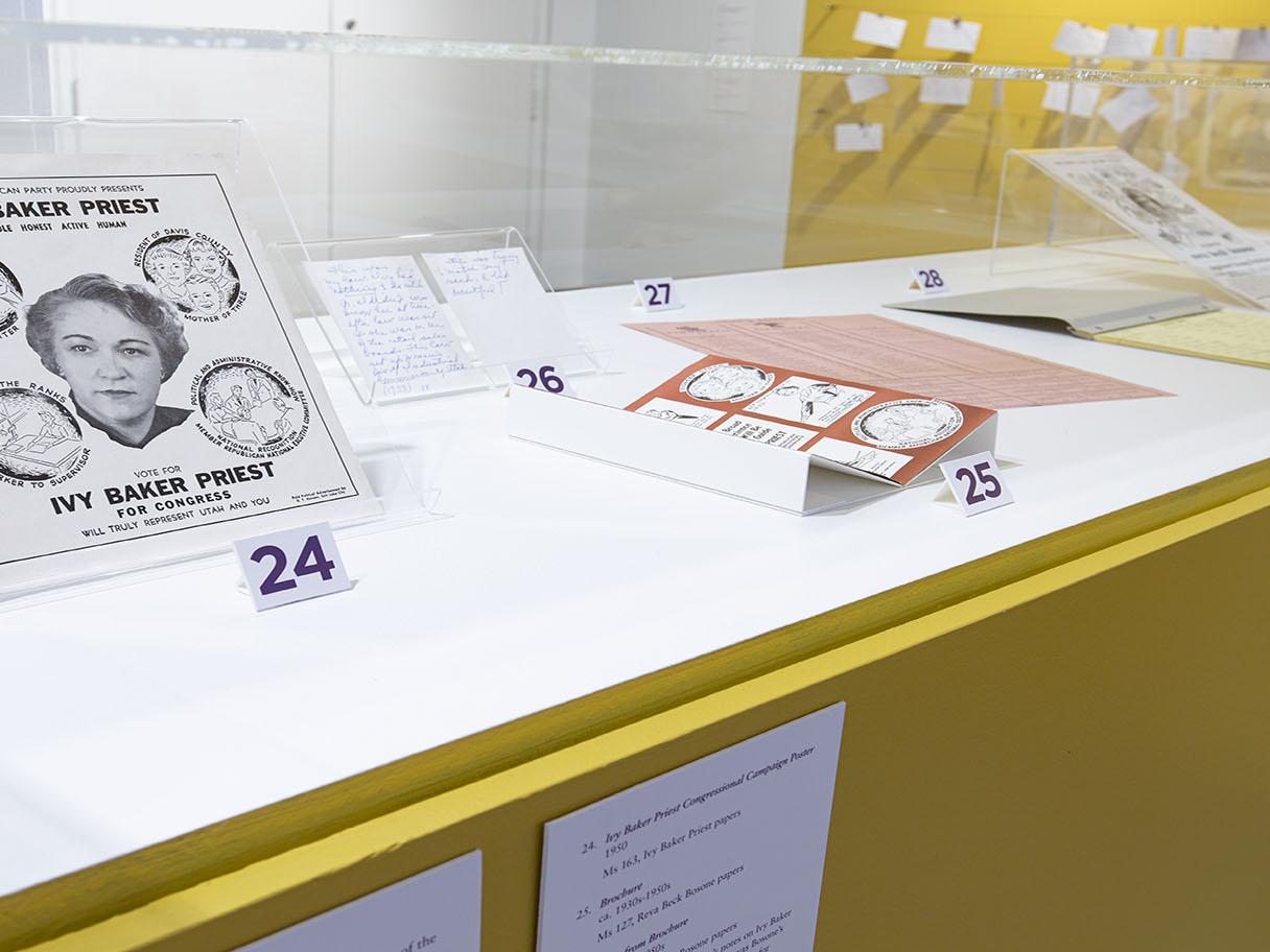 Numbered paper artifacts laid out next to one another in a glass display case with a yellow bottom.