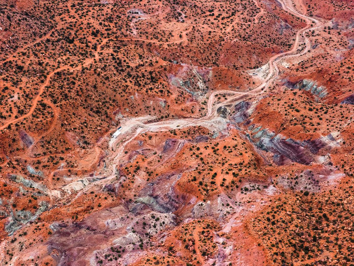 A bird's eye view photo of a rust-colored landscape. You can see mountain tops, greenery and a dried up river bed winding between.