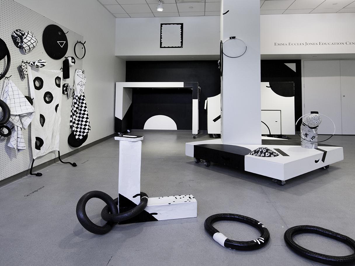 There are random black and white patterned objects strewn about a large white room with concrete floors.
