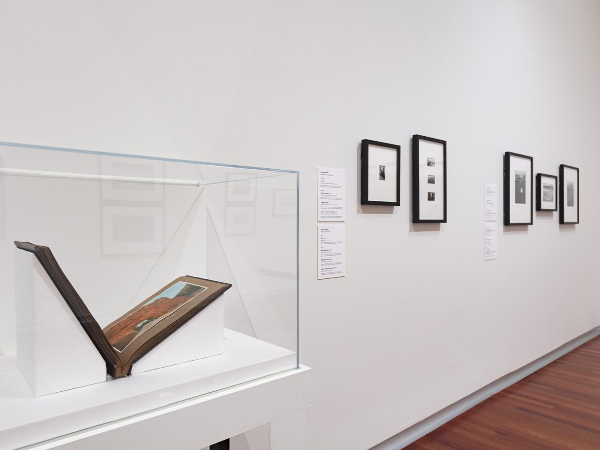 A photo of an open book inside a clear display case. There are framed photos on the white walls in the background of the image.