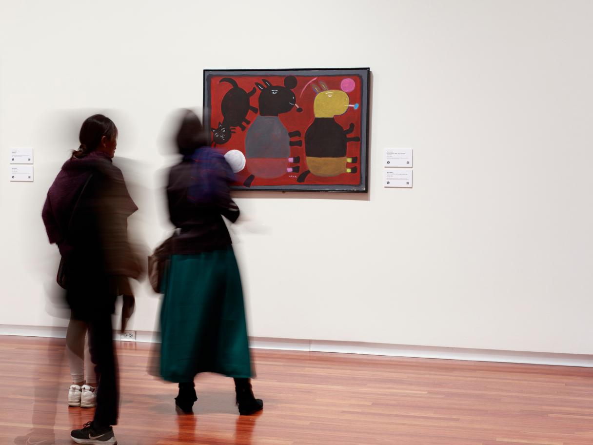 Two blurry figures walk through the gallery.