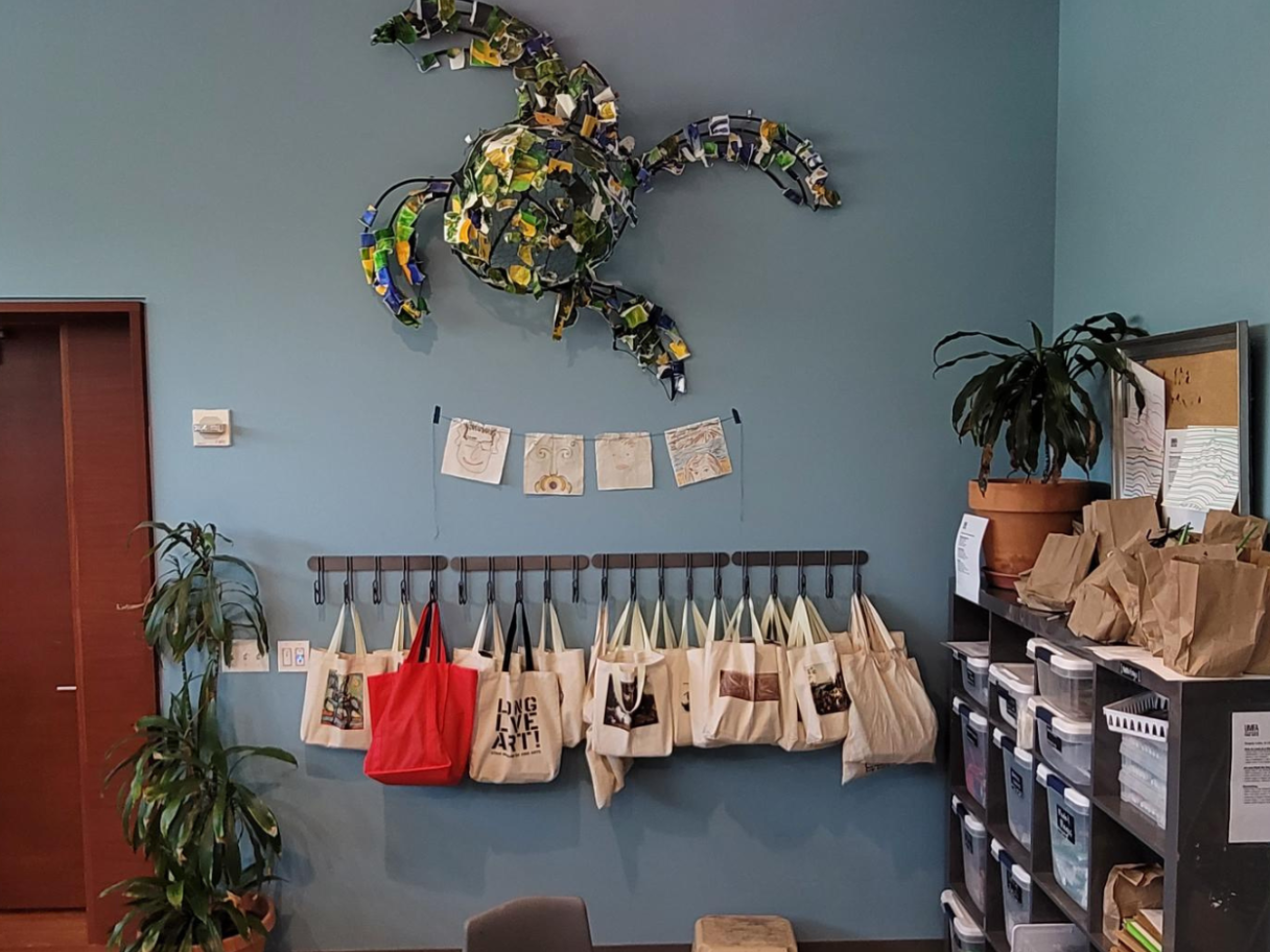 A classroom with a recycled turtle sculpture, a row of tote bags, and a small string of flags on the walls.