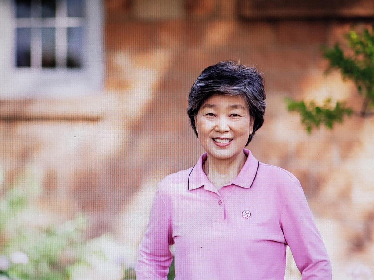 an Asian woman with short dark hair,outside, wearing a long sleeve, collared, pink shirt.