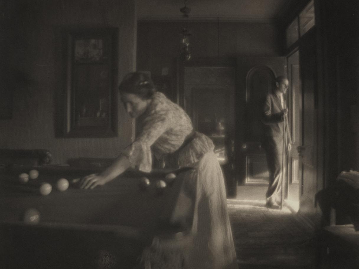 A black and white photograph of a woman playing billiards.