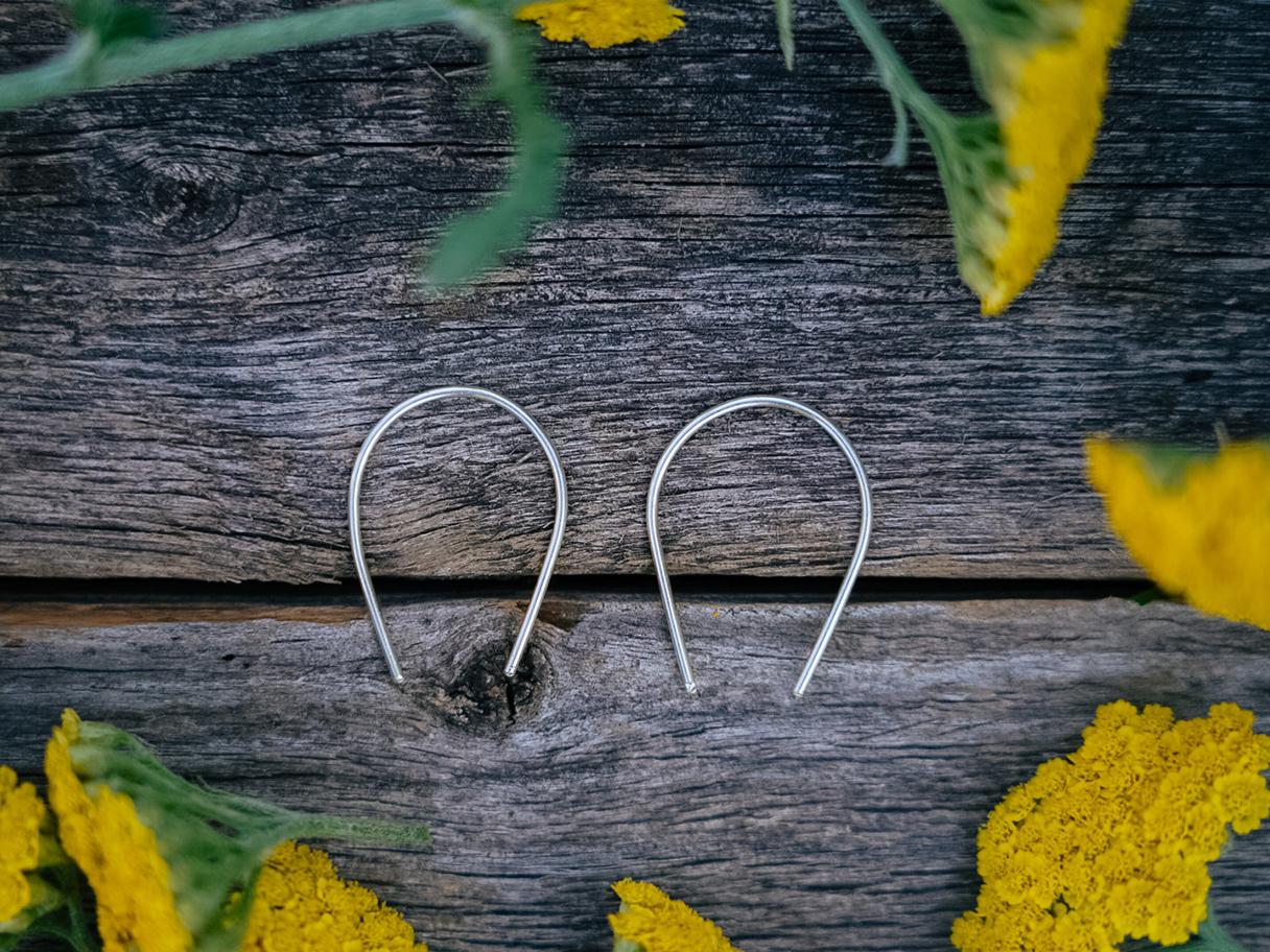 Two small, thin silver jewelry hooks lying flat on a dark wooden table.