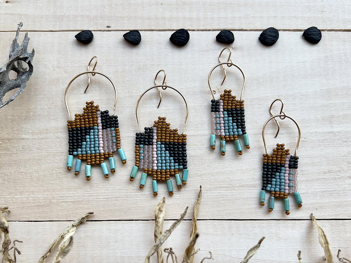 Colorful, intricate beaded earrings on golden hooks, lying flat on a wooden backdrop.