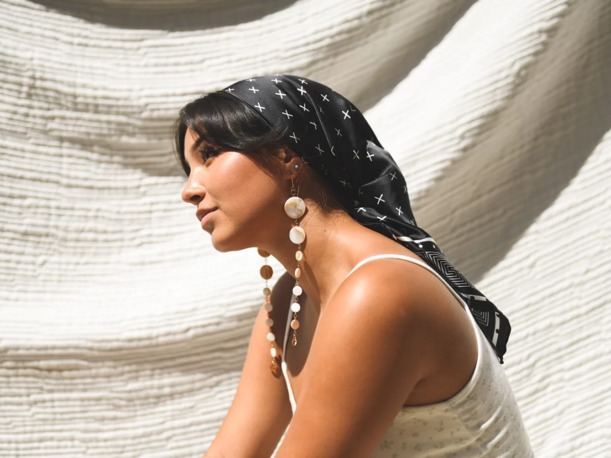 A tan woman with dark long hair, wearing a dark, silky scarf tied around her hair.