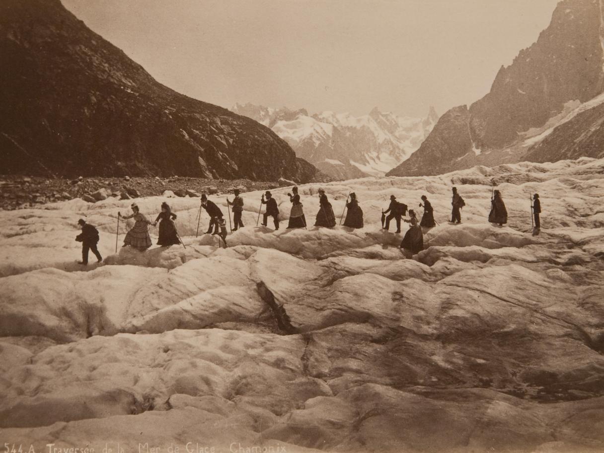 A black and white photograph of a group of people hiking over a glacier.