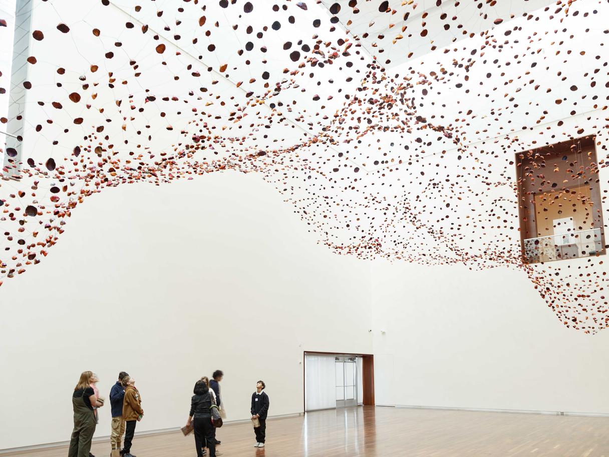 A group of people stand, looking up at thousands of copper foils shaped like rocks, suspended from the ceiling.