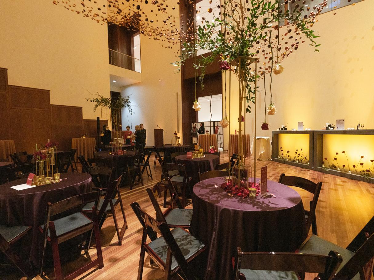 Several round tables with chairs surrounding them are scattered across the Great Hall with floral decor hanging from the ceiling.