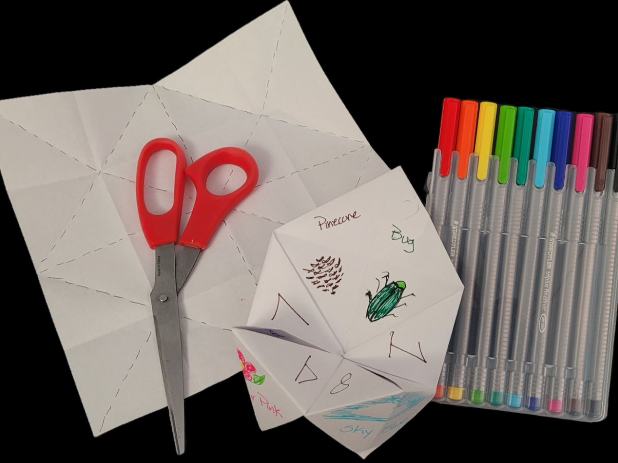 Craft supplies and a 'cootie catcher'. The cootie catcher has numbers and illustrations of nature on it like pine cones, bugs and the sky.