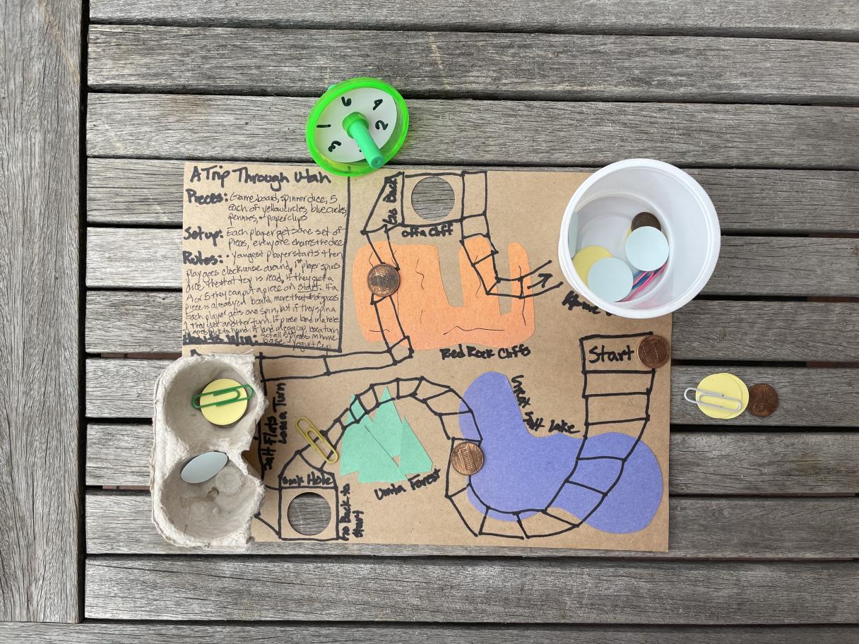 A cardboard game board with colorful recycled pieces.