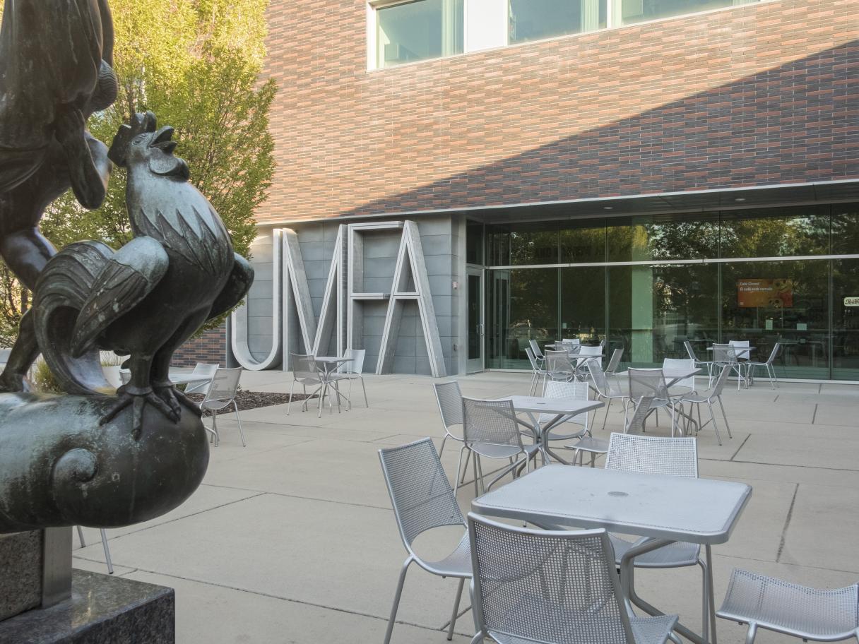 Outdoor patio with multiple tables and chairs, outside Museum building.