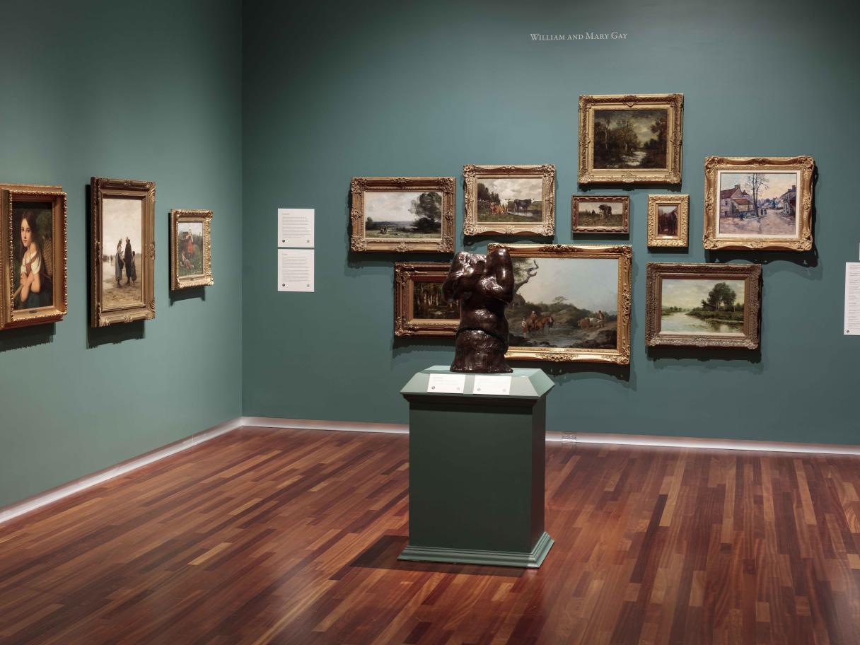 Gallery with several paintings hanging on the wall and a small statue in the center of the room.