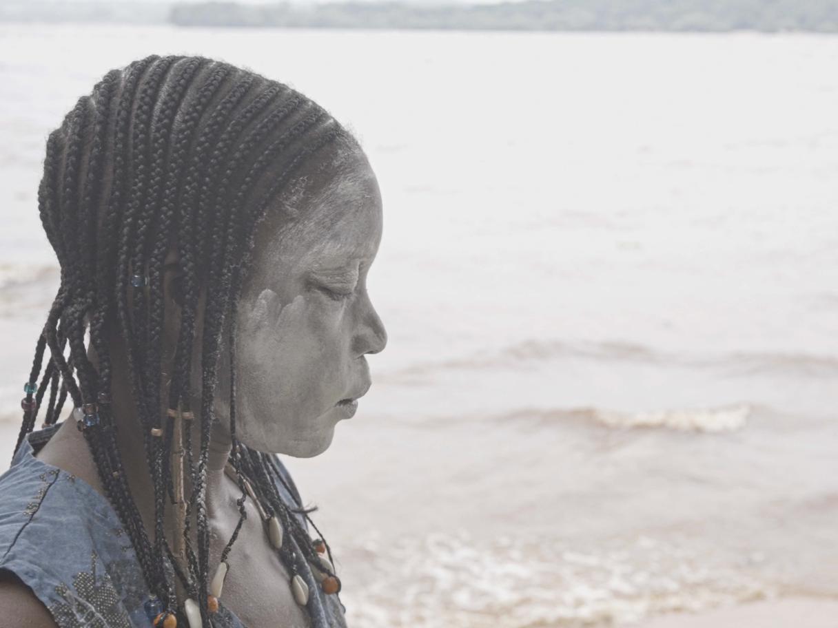 Adama Delphine Fawundu in profile. Gentle waves crash behind her.