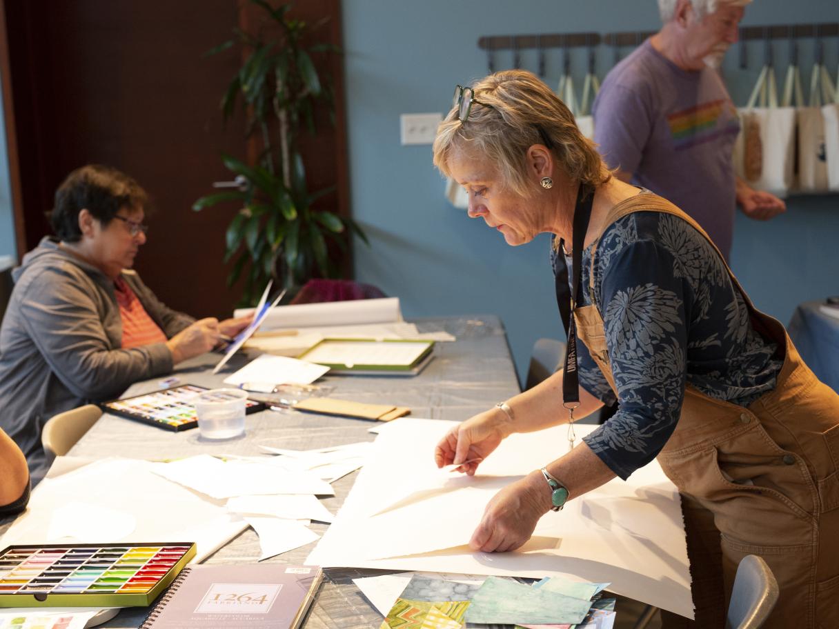 Laura Sharp Wilson bends over a table preparing art making supplies.