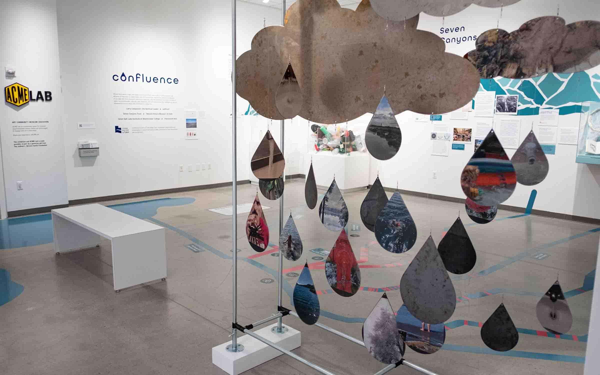 gallery view of Confluence, large sculpture of clouds and exaggerated raindrops made of sheet metal in the foreground 