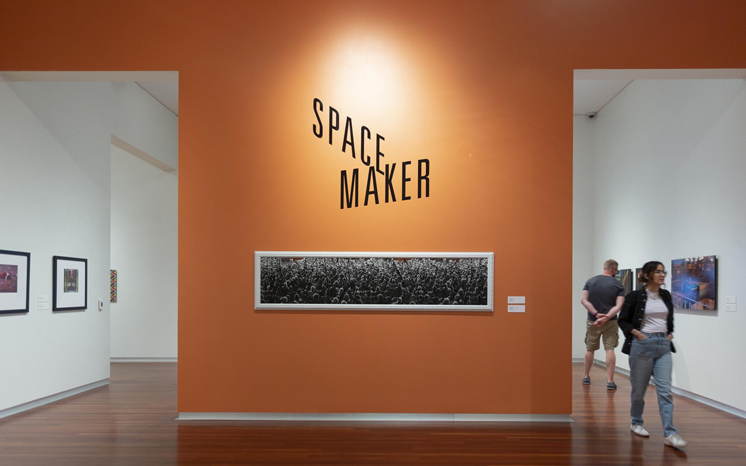 Space Maker orange title wall with a long narrow black and white image under the logo