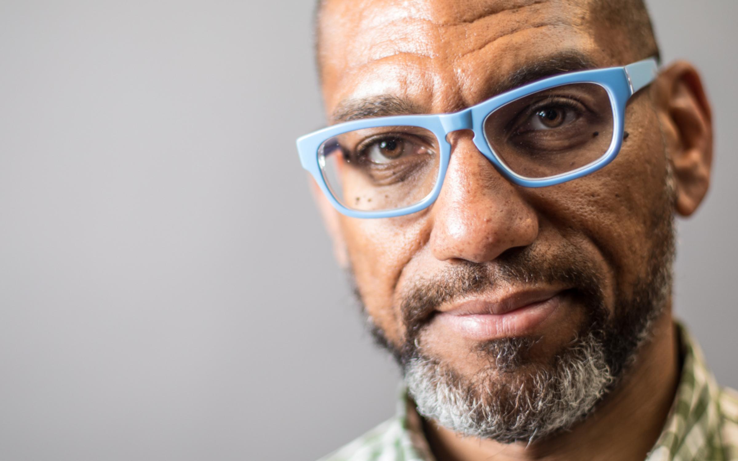 King Britt headshot, a Black man with salt and pepper beard and blue glasses