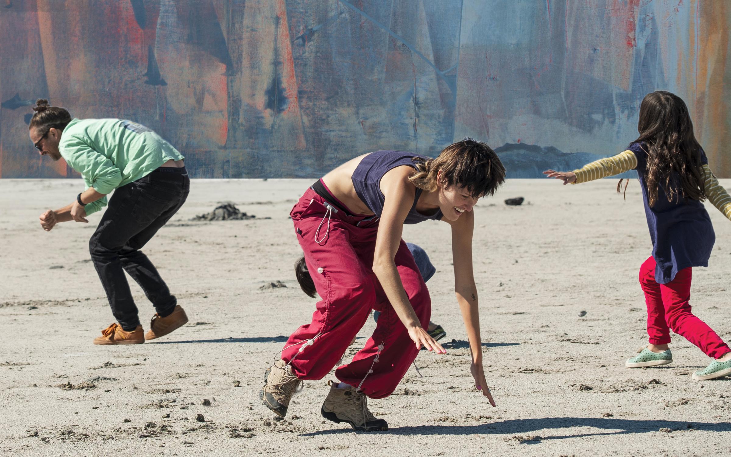 A man, woman, and young child are crouched on a sandy floor with a painting edited in the sky.