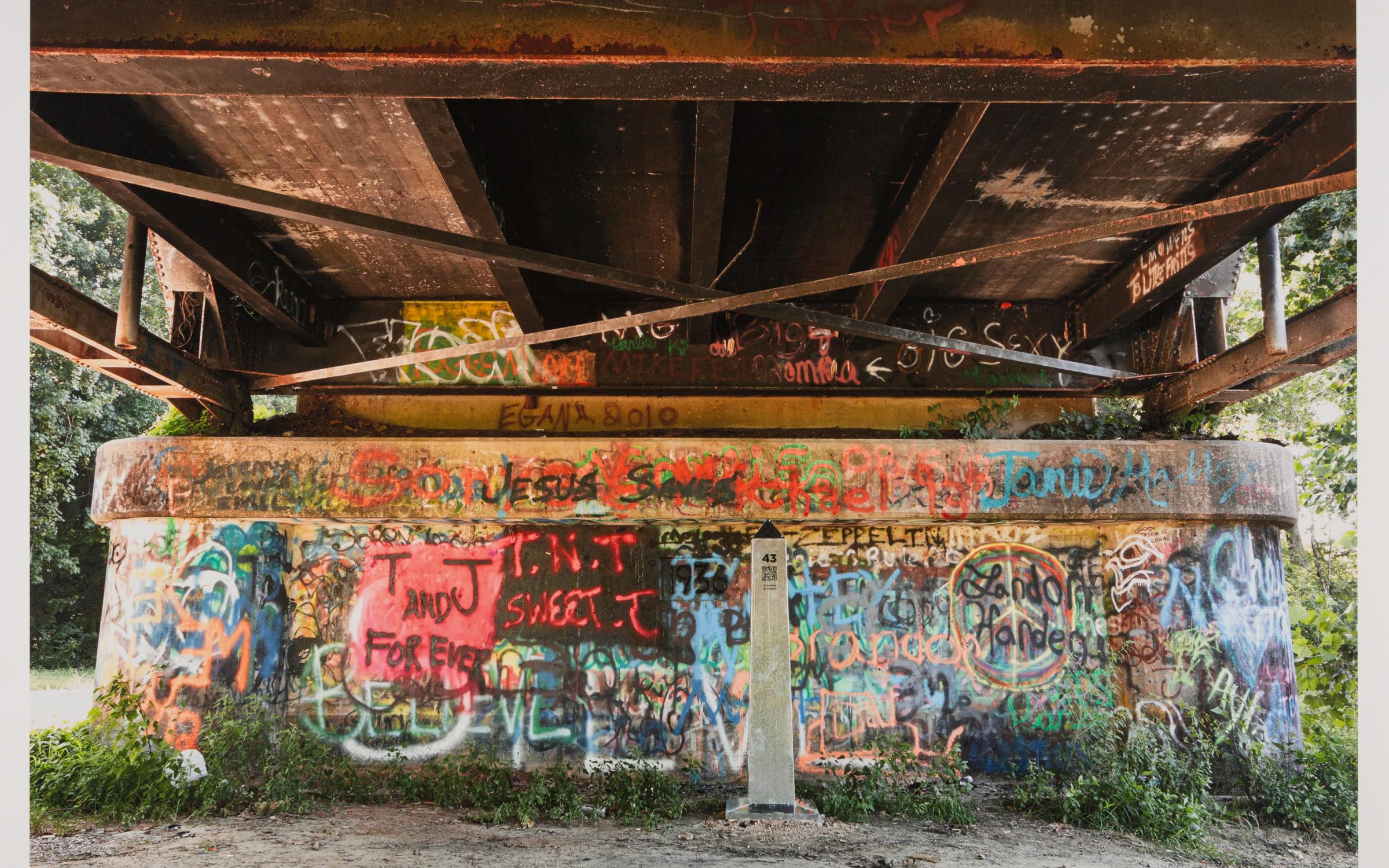 A photo of an obelisk under a bridge with graffiti 