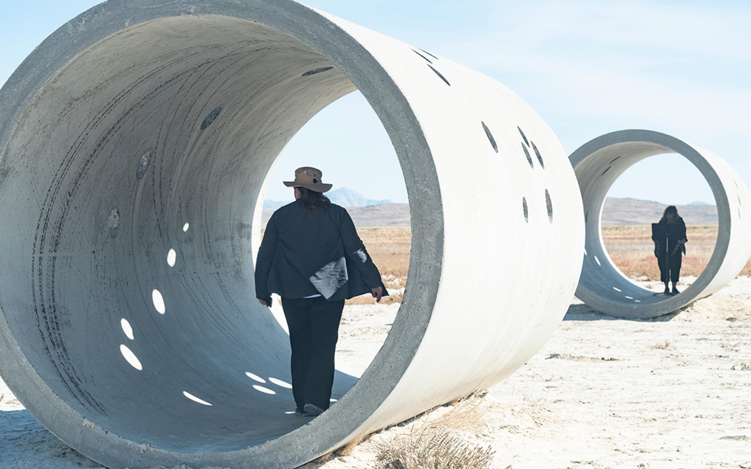 A view of Nancy Holt's Sun Tunnels with a mountain range in the background during sunset.