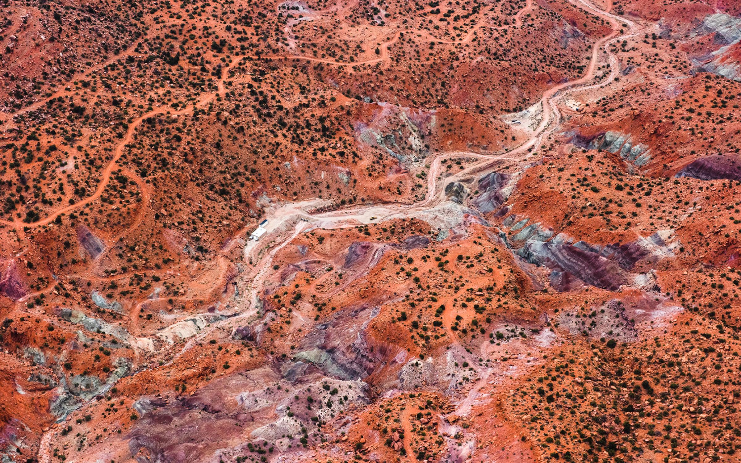 A bird's eye view photo of a rust-colored landscape. You can see mountain tops, greenery and a dried up river bed winding between.