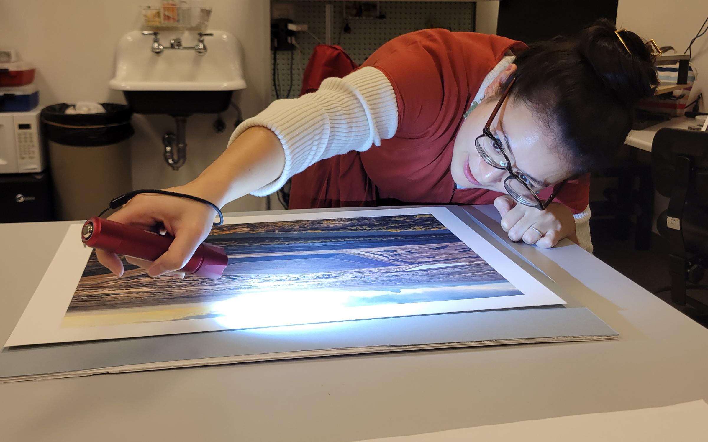 Director of collections, Stacey Kelly uses a flashlight to inspect a piece of art.