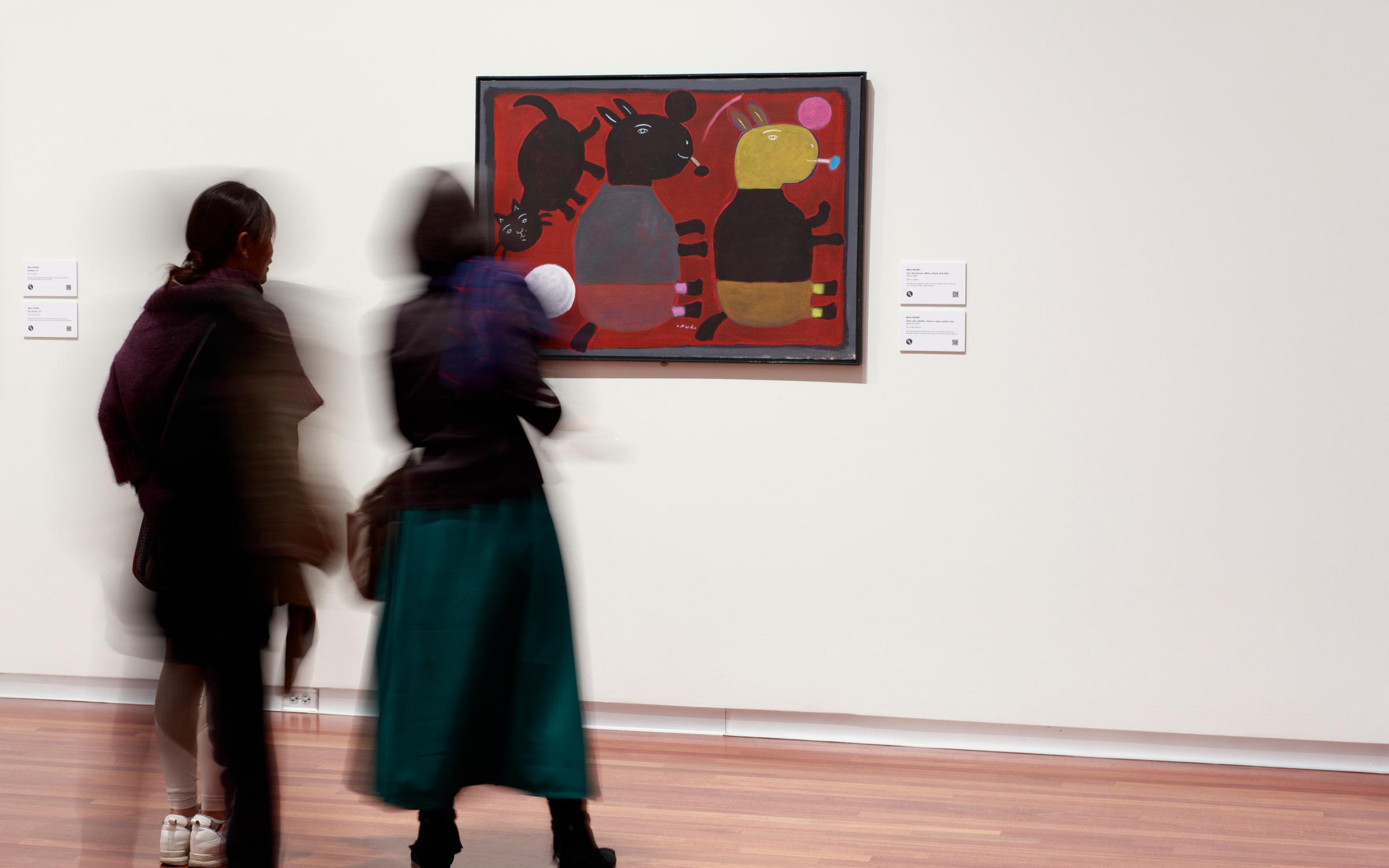 Two blurry figures walk through the gallery.